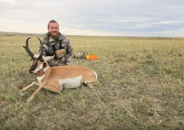 A smiling hunter kneeling behind a pronghorn antelope on the open prairie
