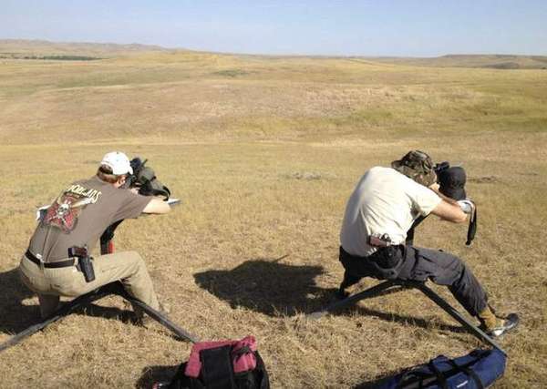 Two shooters set up on shooting benches overlooking rolling prairie